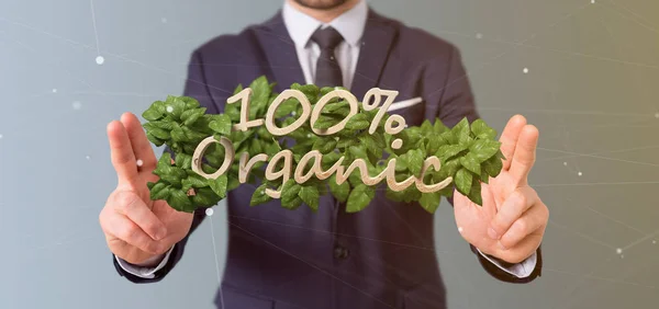 Businessman holding a Wooden logo 100 % organic with leaves arou — Stock Photo, Image