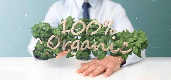 Businessman holding a Wooden logo 100 % organic with leaves arou — Stock Photo, Image