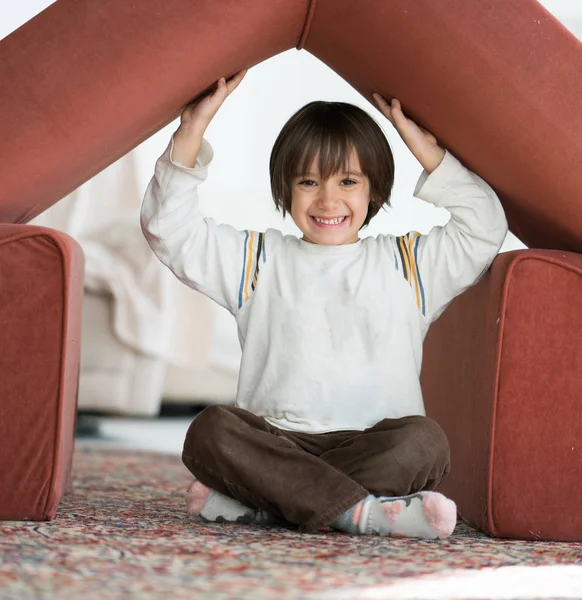 Little boy with long hair playing at home making house with roof — Stock Photo, Image