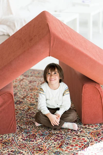 Niño con el pelo largo jugando en casa haciendo casa con techo — Foto de Stock