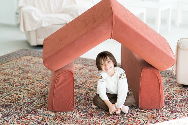 Маленький мальчик с длинными волосами играет в доме делая дом с крышей — стоковое фото