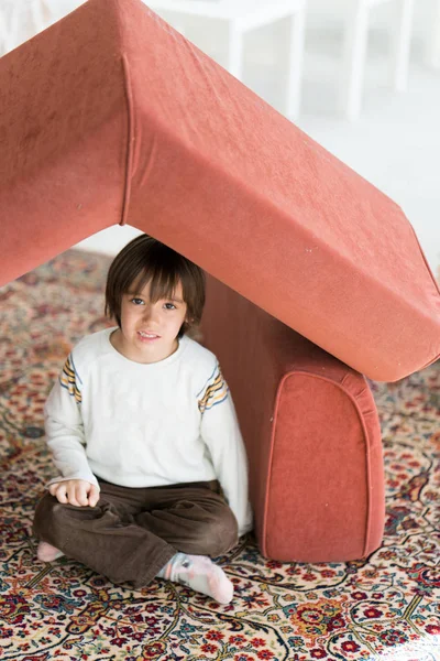 Menino com cabelo comprido brincando em casa fazendo casa com telhado — Fotografia de Stock