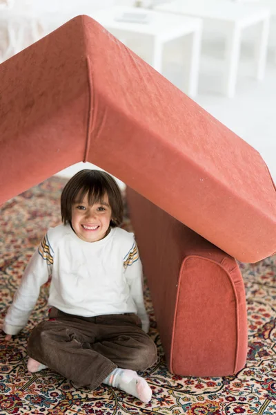 Μικρό αγόρι με μακριά μαλλιά που παίζει στο σπίτι κάνοντας σπίτι με στέγη — Φωτογραφία Αρχείου