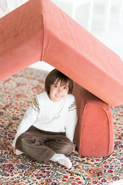 Niño con el pelo largo jugando en casa haciendo casa con techo — Foto de Stock