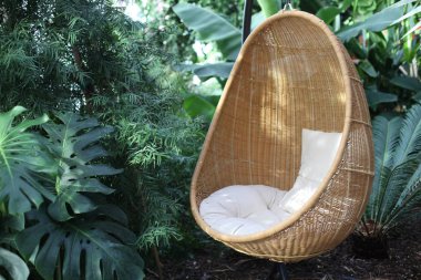Rattan oval sallanan sandalye tropikal bitkide yastıkla.