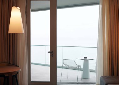 Balkona açılan cam kapılı oturma odası. Deniz manzaralı.