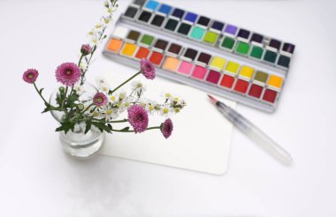 Beyaz kağıt arkaplanda suluboya, fırça ve boş kart ile çiçek. 