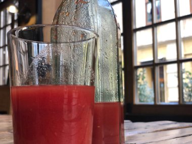 Şişede ev yapımı domates suyu ve kafedeki kaba ahşap bir masada cam..