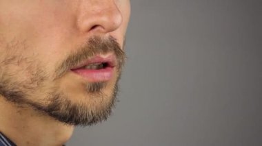adam konuşuyor, closeup erkek ağız ile bir sakal ve bıyık, gri arka plan, yan görünüm, kopya alanı 