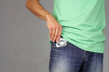 Yeşil tişörtlü adam koyar veya yeni prezervatif cebinde açık mavi kot pantolon, güven ve sorumluluk, gri arka plan, kopya alanı dayalı ilişkiler kavramı dışarı alır