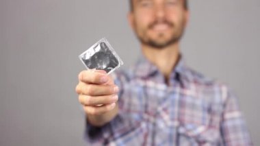 ekose gömlekli adam tutan yeni prezervatif ortasına uzanmış el ve gülümseme, o zaman dediği gibi onun gömlek cep, sağlıklı bir yaşam tarzı ve cinsel ilişkiler, gri arka plan kavramı 