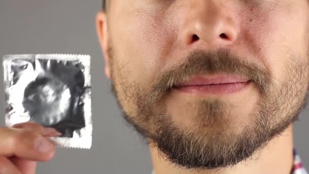 男のひげと口ひげを保持と新しいコンドーム手に彼の顔と笑顔 健康的なライフ スタイルと性的関係 灰色の背景 正面の概念に近い — ストック動画
