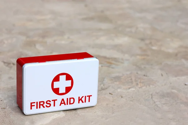 first aid kit box on stone floor, portable medical equipment for travelers, copy space on the right side, close-up
