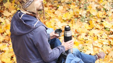 sırt çantası, dikiz, gezi, sarı sonbahar yeşillik zemin üzerine hiking içinde dinlenme ile sonbahar ormandaki adam sıcak içecek - çay veya kahve ve termos bardak ile oturur  