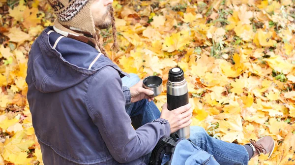 sırt çantası, dikiz, gezi, sarı sonbahar yeşillik zemin üzerine hiking içinde dinlenme ile sonbahar ormandaki adam sıcak içecek - çay veya kahve ve termos bardak ile oturur  