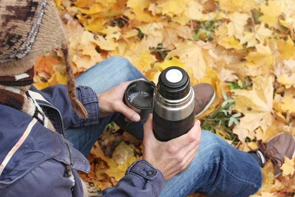 秋の森 上部背面に黄色の紅葉の背景に ハイキングの残りの部分に座っているホットド リンク ポットとコーヒー 紅茶のカップを持つ男 — ストック写真