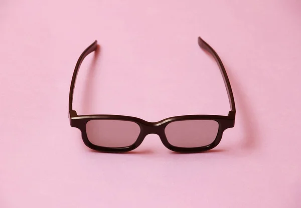 single black plastic cinema 3d glasses on coral pink background, temple arm of eyeglasses are open, closeup