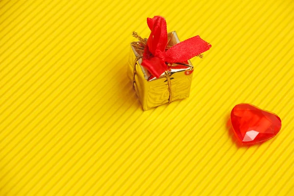 Gold present or gift box with red bow and ribbons and red plasst — Stock Photo, Image