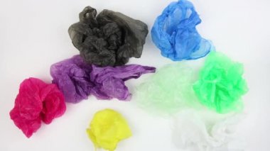 farklı renklerde buruşturulmuş kullanılan plastik torbalar kaotik beyaz arka plan, üst görünüm, closeup, stopmotion animasyon, büyük ekolojik sorun döner