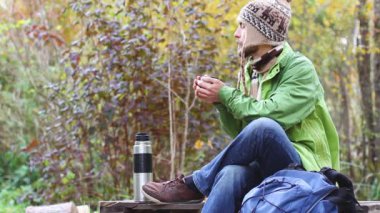 sakallı hipster bin yıllık adam oturan bacaklarını geçti, ellerini ısıtır ve fincan sıcak çay veya kahve içecekler, rüyalar, gülümseme ve doğa güzelliği, yan görünüm, kupa buhar zevk, sarı sonbahar  