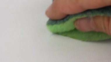 insan eli dikkatle yeşil bir bulaşık yıkama süngeri ile masanın beyaz yüzeyi siler, closeup