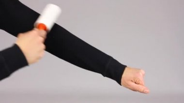 adam nazikçe temizleyin bez için yapışkan rulo ile siyah giysi kol temizler, yukarı ve aşağı, gri arka plan taşır