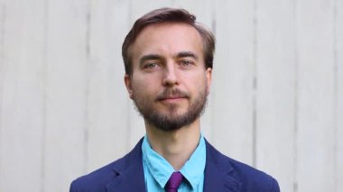 bir takım elbise ve kravat içinde traşsız genç adam, çerçevenin ortasında gülümseyerek