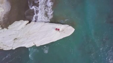 Kalymnos veya Kıbrıs Vali Plajı beyaz taş pelerin üzerinde ailenin havadan görünümü, kırmızı gömlekli baba anne ve oğlu deniz kıyısında oturur, seyahat ve tatil, yukarıdan dikey çekim