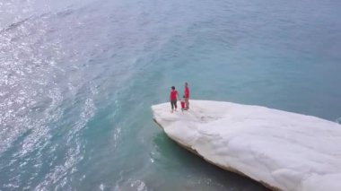 Kalymnos veya Kıbrıs Vali Plajı beyaz taş pelerin üzerinde aile rekreasyon havadan görünümü, kırmızı gömlekli baba anne ve oğlu deniz kıyısında eğlenmek, insanlar seyahat, drone kamera etrafında sinek   