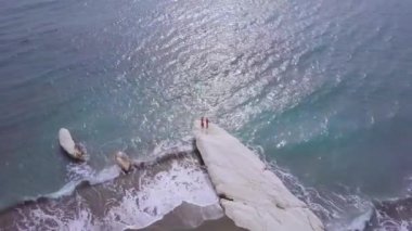 Kalymnos veya Kıbrıs Vali Plajı beyaz taş pelerin üzerinde aile rekreasyon havadan görünümü, kırmızı gömlekli baba anne ve oğlu ellerini dalgalar, deniz kıyısı, drone kamera etrafında sinek   