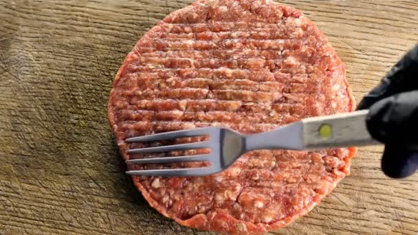 Cuoco cuoco in guanti neri forma una cotoletta per cucinare con una forchetta sulla cotoletta, l'ingrediente principale per un hamburger, primo piano vista dall'alto — Video Stock