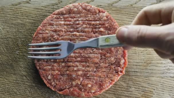 Côtelette ronde brute posée sur une planche de bois et sur laquelle elle est tenue à l'aide d'une fourchette formant des hamburgers, filmant par le haut — Video