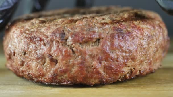 Gegrilde kotelet ligt op een houten plank, de chef-kok in zwarte handschoenen pakt de kotelet op om een hamburger te vormen — Stockvideo