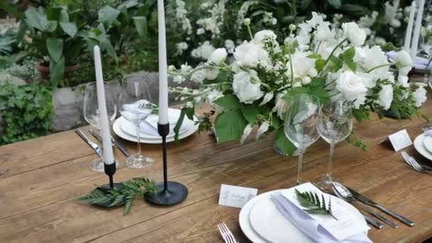 Vacker dekor av ett gammalt träbord för en bröllops kväll i rustik stil med blommiga buketter och ljus — Stockvideo