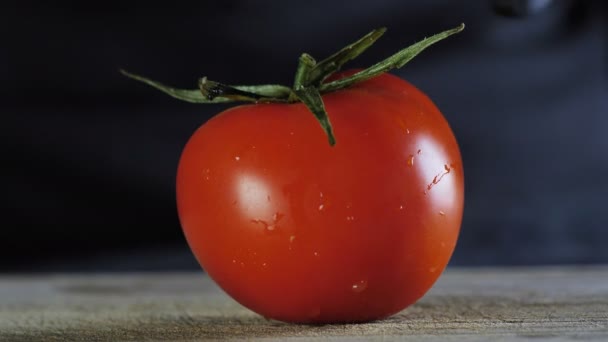 Um tomate grande encontra-se em uma placa de madeira em um fundo isolado preto, o chef corta um tomate em duas partes — Vídeo de Stock