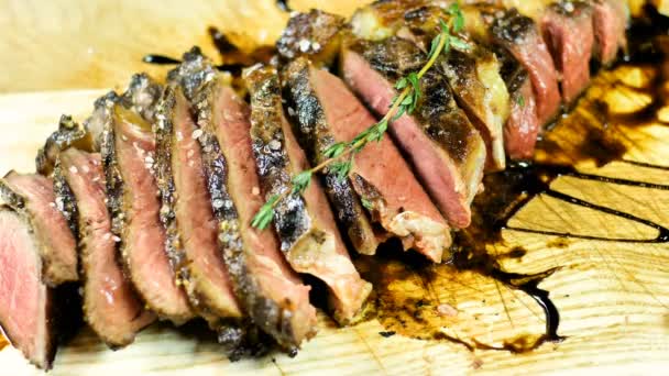 Nahaufnahme von gegrilltem Steak in dünne Scheiben geschnitten auf einem Holzbrett mit einem Zweig Rasmarin dekoriert ist mit Gewürzen und Salz gepflanzt — Stockvideo