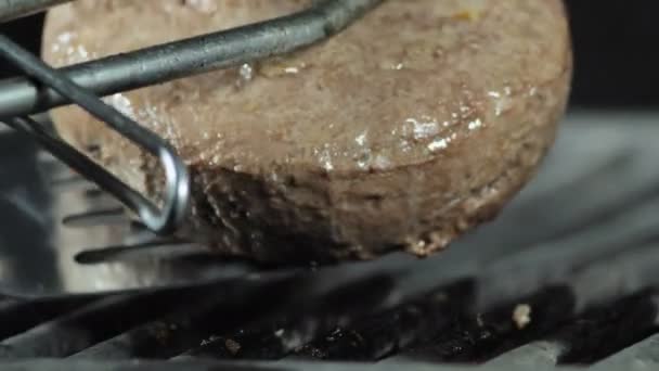Ένα μεγάλο ζουμερές Burger Burger είναι ψητό κοντινό-up, με λαβίδες σιδήρου για να μετατρέψει το πατάκι στην άλλη πλευρά για περαιτέρω μαγείρεμα — Αρχείο Βίντεο