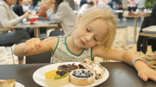 Meisje eten geassorteerde taarten in een café op een onscherpe achtergrond. — Stockvideo