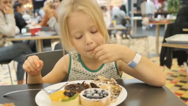 Baby girl tries assorted cakes in a cafe — Stock Video