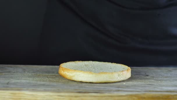 Gros plan sur le début de la formation d'un hamburger, la moitié du pain de hamburger tombe sur une planche de bois et puis une feuille de laitue tombe dessus — Video