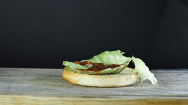 Nahaufnahme eines halben Brötchens für einen Burger mit einem Salatblatt, auf das Tomatensauce gegossen wird — Stockvideo