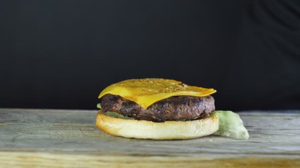 Gros plan d'un demi-pain pour un hamburger avec une escalope de laitue sur le dessus et deux tranches de fromage frit avec un brûleur à gaz sur le dessus, le chef tartiner la moitié suivante du pain, un grand méga hamburger — Video