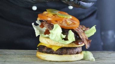Sebze ve susam topuzun ile çift pirişlet ile Mega büyük burger, bir burger oluşturma süreci, siyah eldiven şef burger üst katmanı üzerinde salatalık turşusu dilimleri yayılır