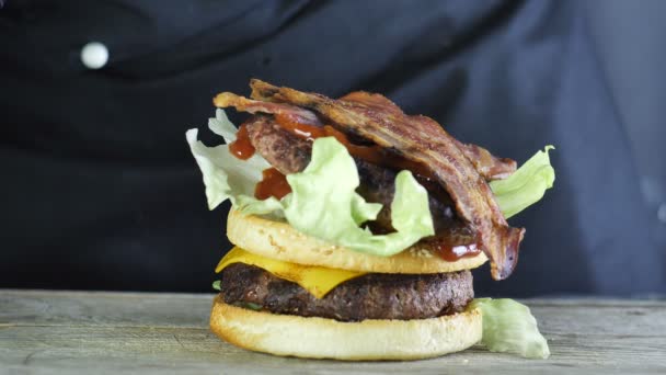 Primer plano de medio bollo para una hamburguesa con chuletas de lechuga en la parte superior y dos rebanadas de queso frito con un quemador de gas en la parte superior más otra mitad del bollo en el que una nueva capa de lechuga y chuleta con — Vídeo de stock