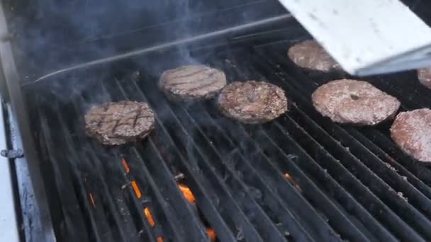 Cozinhar hambúrgueres de hambúrguer e cheeseburgers em uma chama de uma carne de grelha de jusper de carne de porco bateu vitela e filetes de frango de uma comida de rua de festa. Borrifos de gordura estão voando, costeletas de churrasco são — Vídeo de Stock