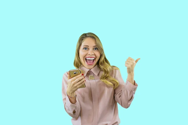 Attractive and joyful blond girl in a shirt looks up and holds the phone in her hand against an isolated background — Stock Photo, Image