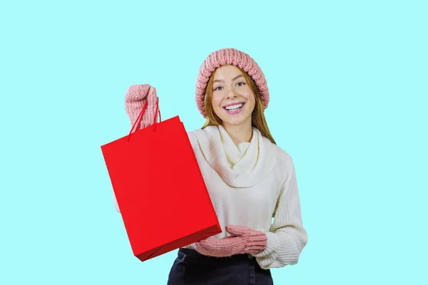 Portret van een schattig roodharige meisje in een gebreide muts en wanten met een rode zak en kijken naar de camera tonen een geschenk op een geïsoleerde achtergrond, mode schieten, nieuwe jaar geschenken — Stockfoto