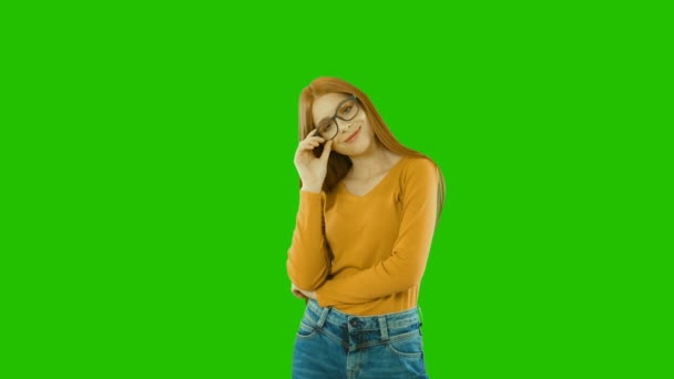 Mladá, krásná zrzavá dívčí školka, studentka v brýlích s pokojným pohledem se dotýká jejích brýlí a úsměvů, zelené pozadí — Stock video