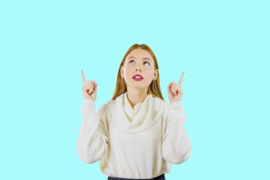 Çekici oldukça kızıl saçlı kız yukarı bakar ve izole bir arka plan üzerinde boş alanda parmak işaret.