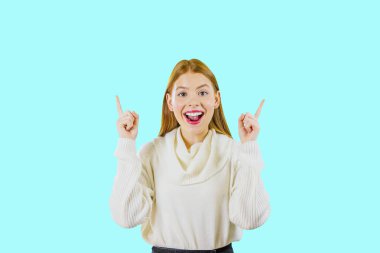 Uzun kızıl saçlı genç bir güzel kız iki işaret parmakları kadar kaldırdı ve ağzı geniş açık kameraya bakarak gülümsüyor, zafer hissi ve sürpriz neşeli duygular